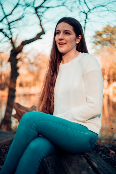 Wearing a white long sleeve shirt and blue denim jeans lady sitting in a brown wooden bench and watch the game
